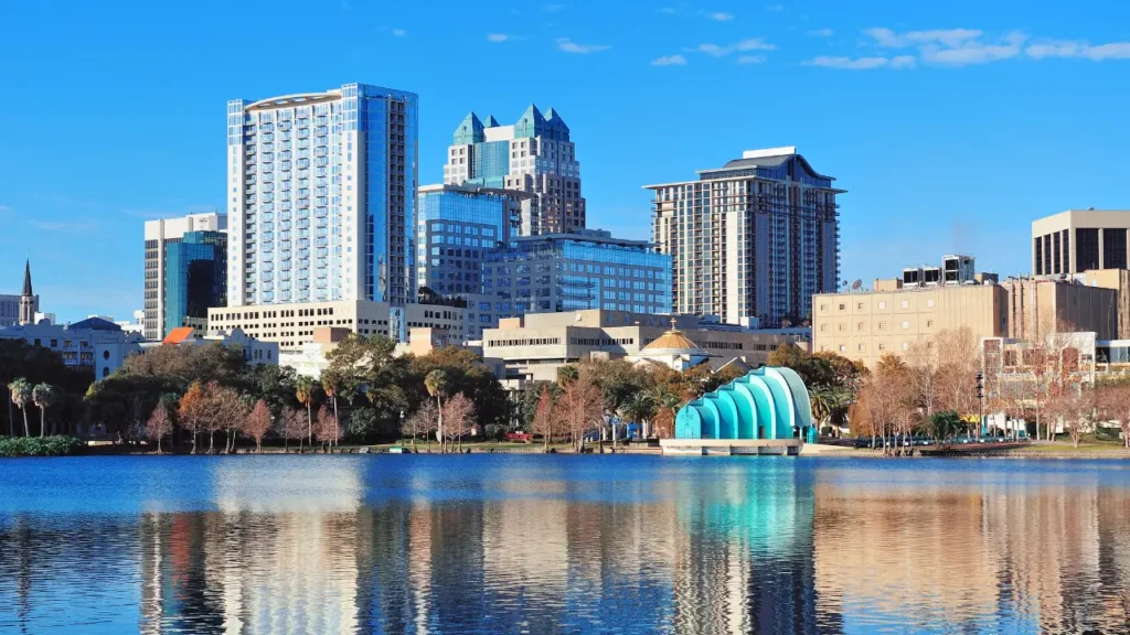 Downtown Orlando skyscrapers and the turquoise Walt Disney Amphitheater reflected in Lake Eola under a blue sky