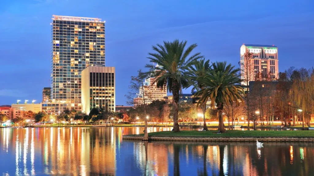 High-rise buildings in downtown Orlando lit up at dusk with a swan swimming on Lake Eola in the foreground