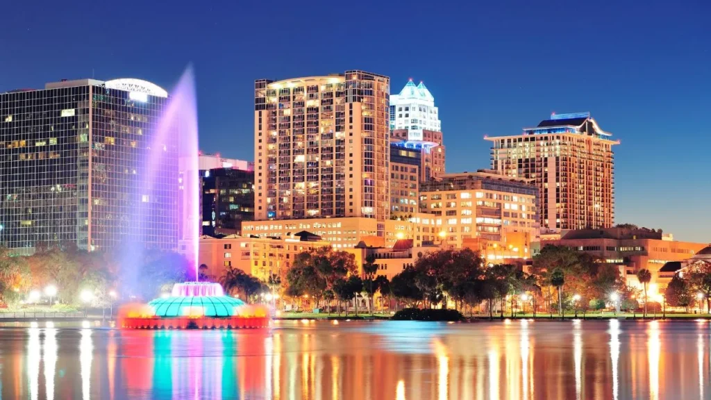 Downtown Orlando skyline at night with the illuminated Lake Eola fountain shooting a colorful water jet into the sky