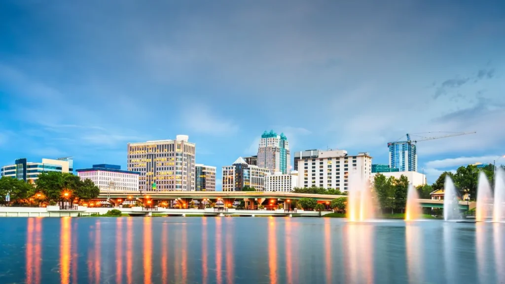Downtown Orlando skyline at blue hour with illuminated fountains spraying water in the foreground and a construction crane in the background