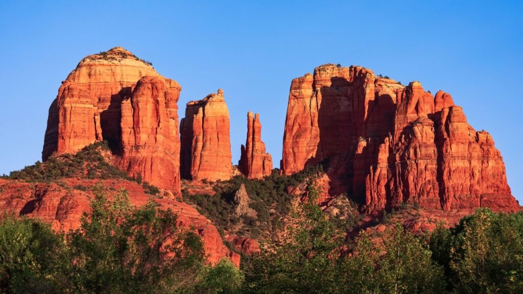 Cathedral Rock reflected in Oak Creek, Sedona, Arizona, surrounded by lush green trees.