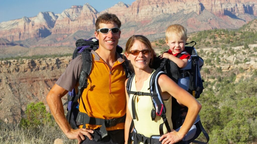 Family hiking in Sedona, Arizona with backpacks and a toddler carrier, red rock mountains in background.