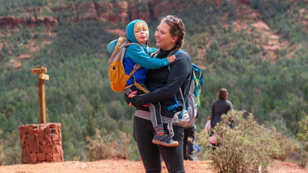 Mother holding child on a Sedona, Arizona hiking trail, with a wooden trail sign in the background.