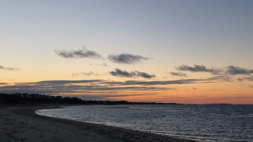 Nantucket beach at dusk with a colorful orange and blue sunset sky over calm ocean water.