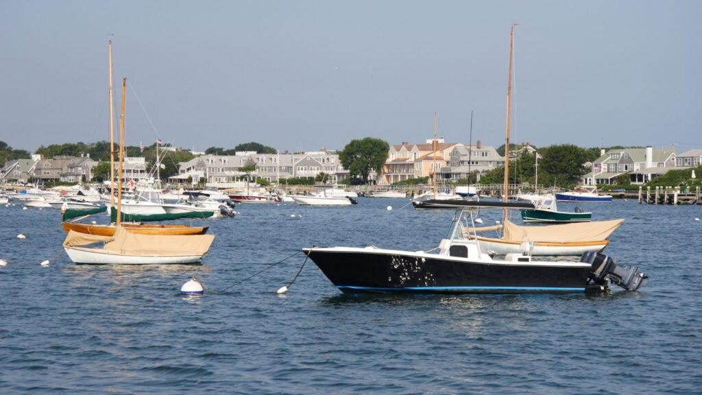 Gray shingled waterfront cottages with American flags overlooking a sailboat in Nantucket Harbor