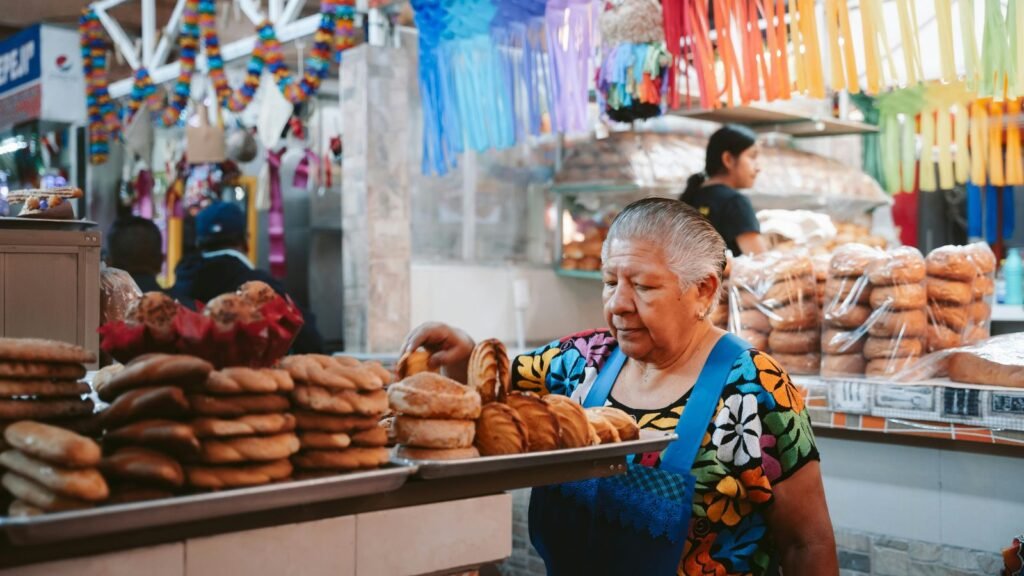 Woman selling traditional pan dulce sweet bread at a market stall in Oaxaca, Mexico, decorated with colorful papel picado