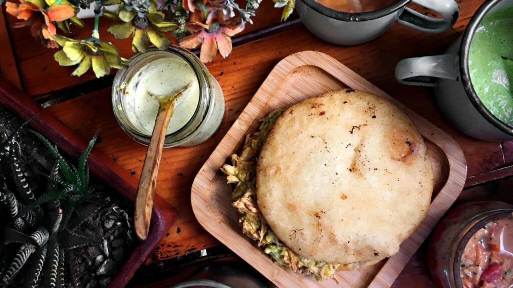 Traditional Venezuelan arepa served on a wooden plate with savory filling and assorted condiments