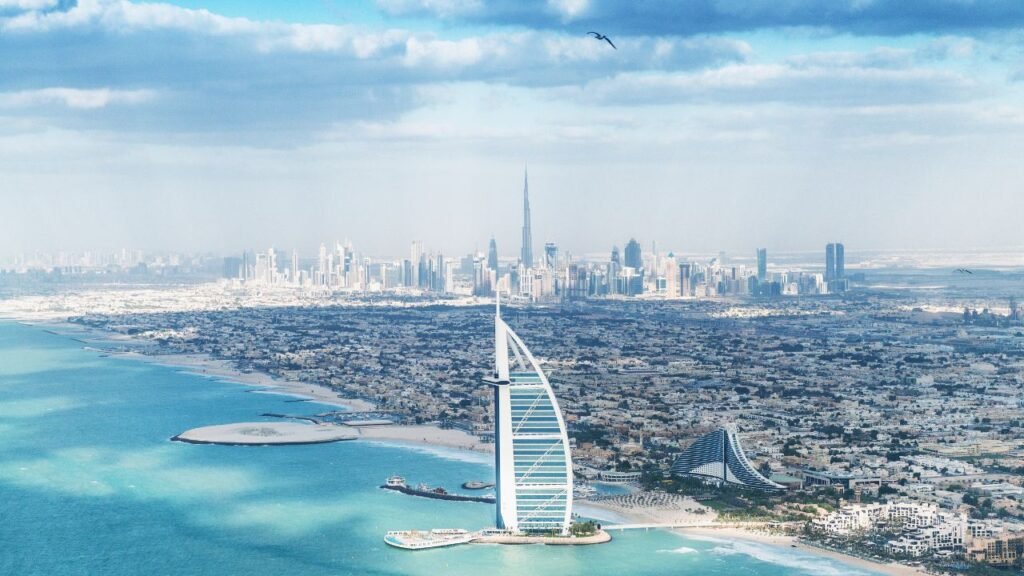 Dubai Marina skyline with a cluster of high-rise towers along the waterfront under a partly cloudy sky, with paragliders visible in the air.