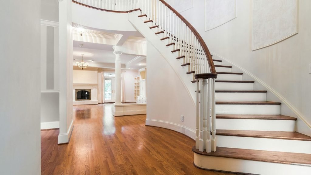 An elegant foyer featuring a curved staircase with wooden treads and white balusters, leading into a spacious, open-concept living room with a fireplace and hardwood floors.