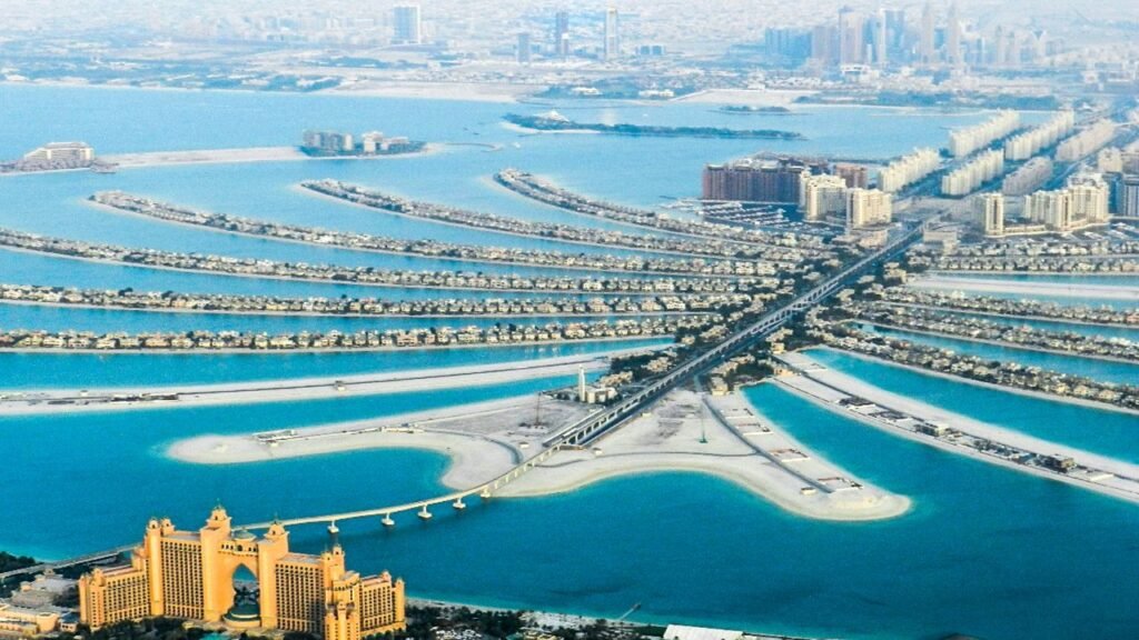 Aerial view of the Palm Jumeirah artificial island with its palm-tree-shaped fronds, villas, and the Atlantis hotel at the base, surrounded by turquoise water