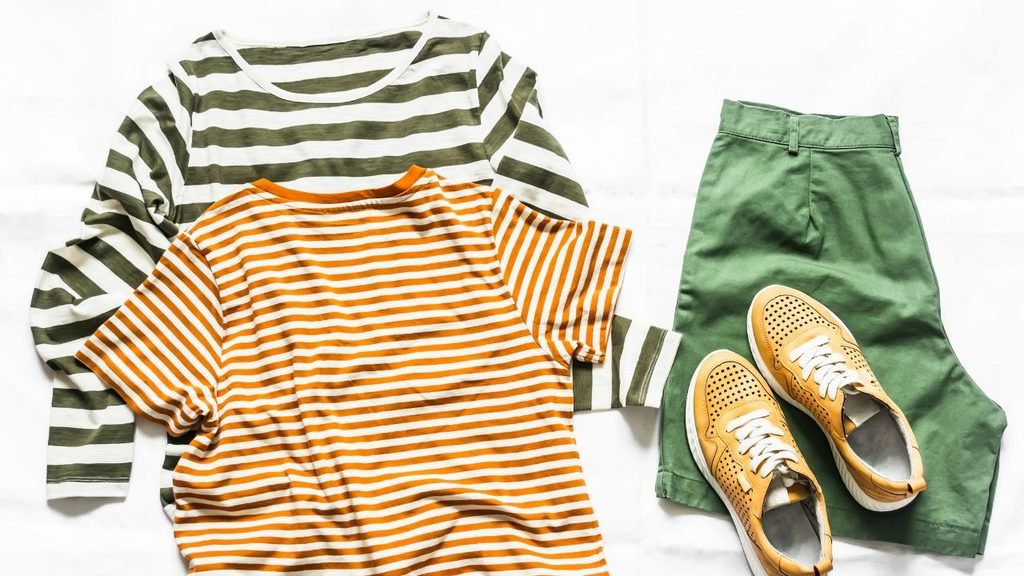Flat lay of striped t-shirts, green shorts, and tan sneakers on a white background
