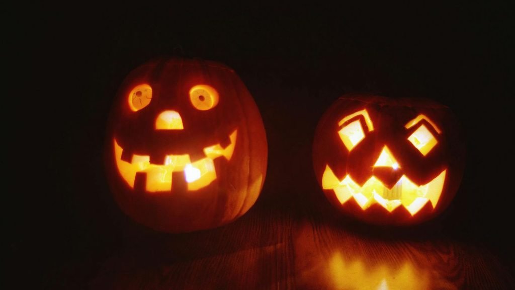 Two illuminated carved pumpkins with different facial expressions glowing in the dark on a wooden surface