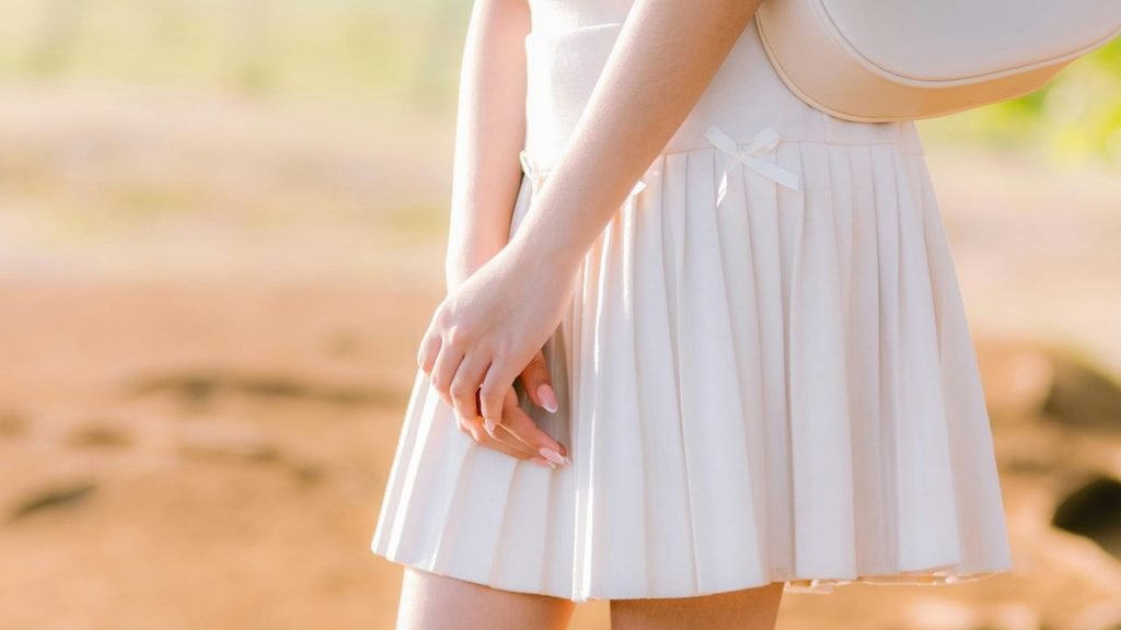 Close-up of a white pleated mini skirt with a small bow detail, paired with a beige crossbody bag