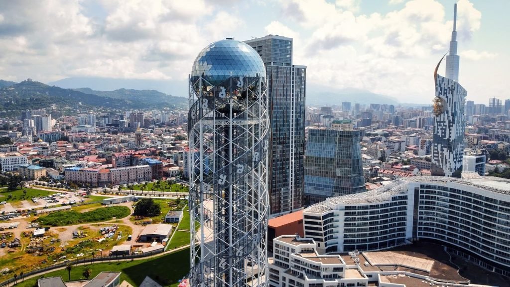 Aerial view of the Alphabetic Tower's glass sphere among Batumi's modern skyscrapers and coastline