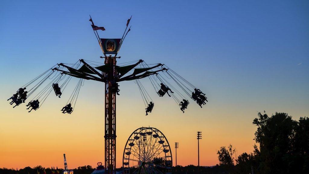 Silhouette of swing ride and Ferris wheel against orange sunset sky at Batumi amusement park